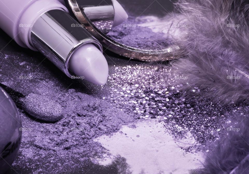 Assorted cosmetics, glitter and feathers in hues of purple, lavender and lilac 