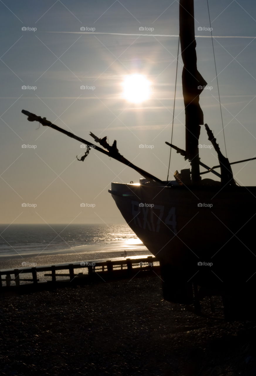 Fishing boat mostly in silhouette against the sun, which shines over the coast of the English Channel in Hastings, UK