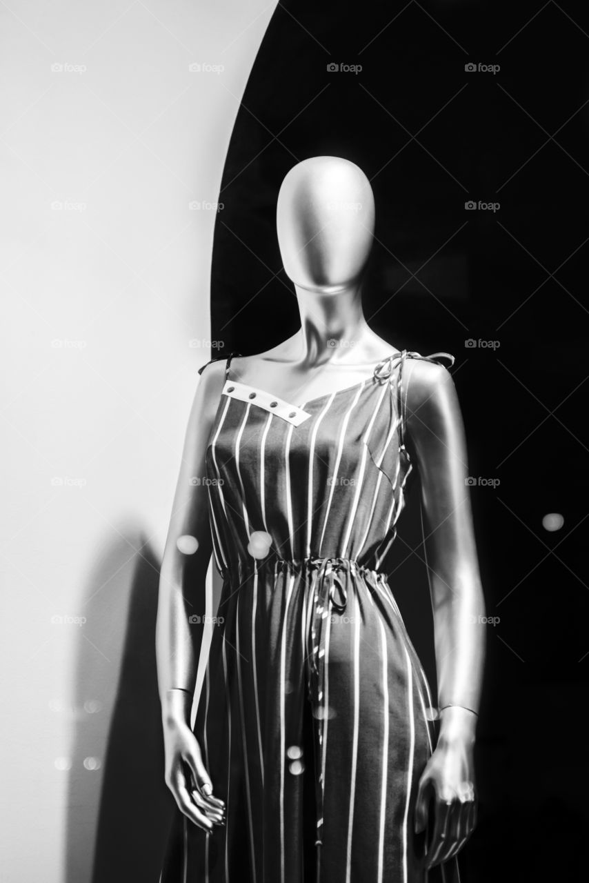 Mannequin standing in store window display of women's casual clothing. Close-up of a plastic mannequin. Black and white