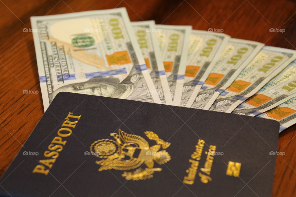 ready to take a weekend vacation. 8 $100 bills with a passport on a brown wooden table.