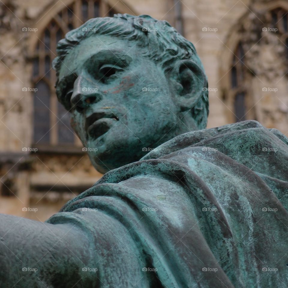 An old copper statue turned a beautiful green of a Roman figure in front of a gothic church in England. 