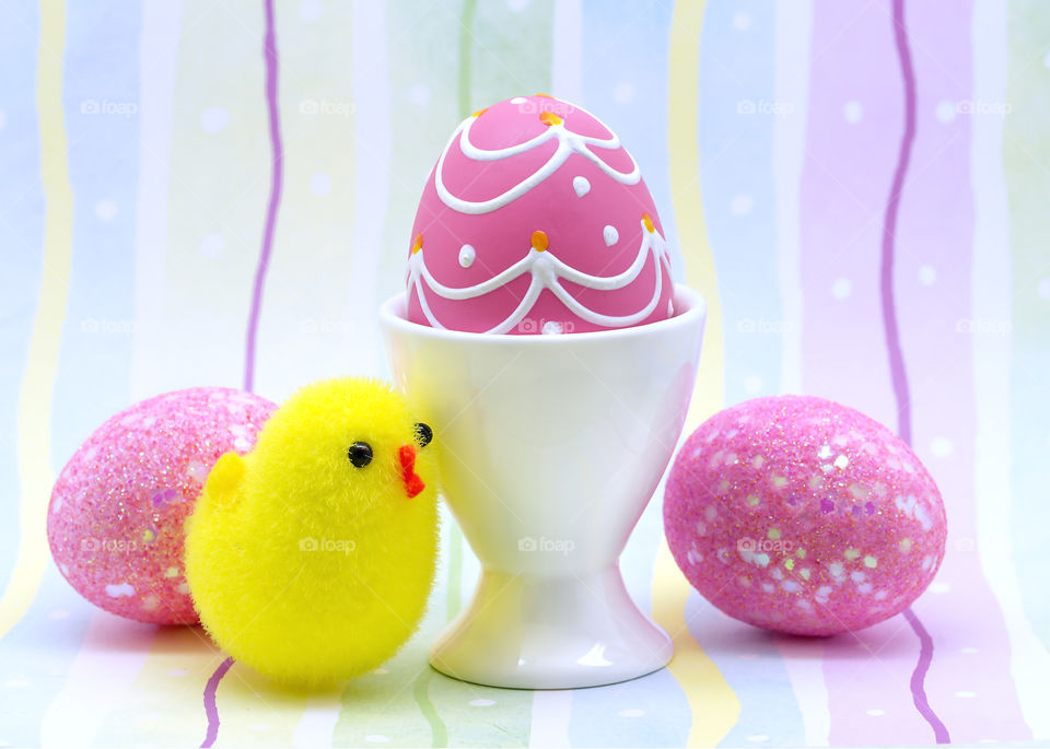 A pink decorated Easter egg in a white eggcup with two pink glitter Easter Eggs and a yellow chicken.