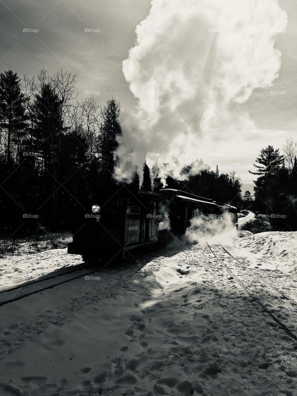 A historic steam engine from the Wiscasset, Waterville & Farmington Railway in Maine, showcasing its impressive vintage design. The locomotive features a large, polished black engine and a prominent smokestack billowing steam.
