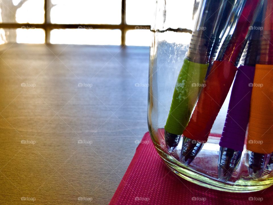 Glass jar of colorful pens on wooden drafting table 