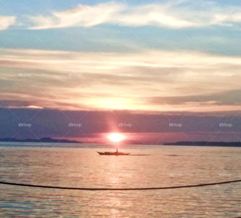 Navigating alone with a small boat made of wood with a natural artwork painted in the sky and beautiful Sunset.