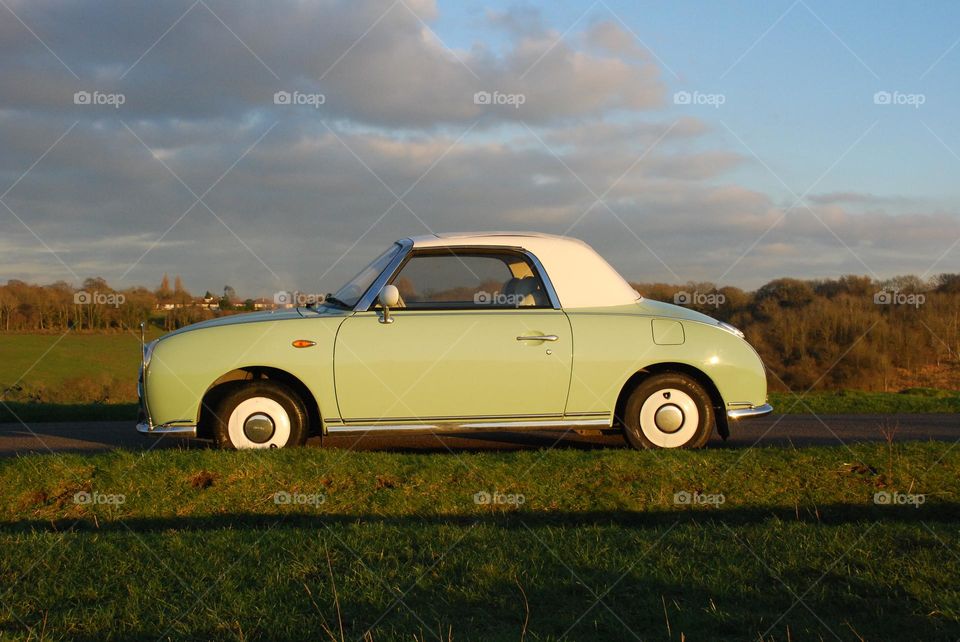 Green and white classic car in the sunshine as the sun begins to set with trees in the distance glowing in the evening sun