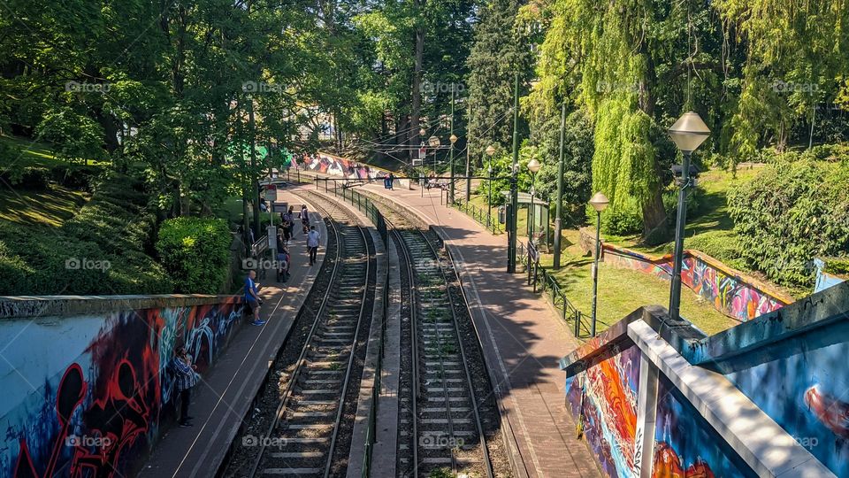 A beautiful view of the tram tracks with a left turn coming out from under the bridge with green trees in the park on the sides on a clear sunny summer day, a close-up view from the bridge from above. The concept of beautiful backgrounds and wallpape