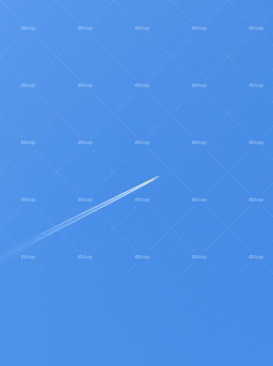 A simple photo of a clear blue sky with an airplane crossing it and leaving a white streak behind it