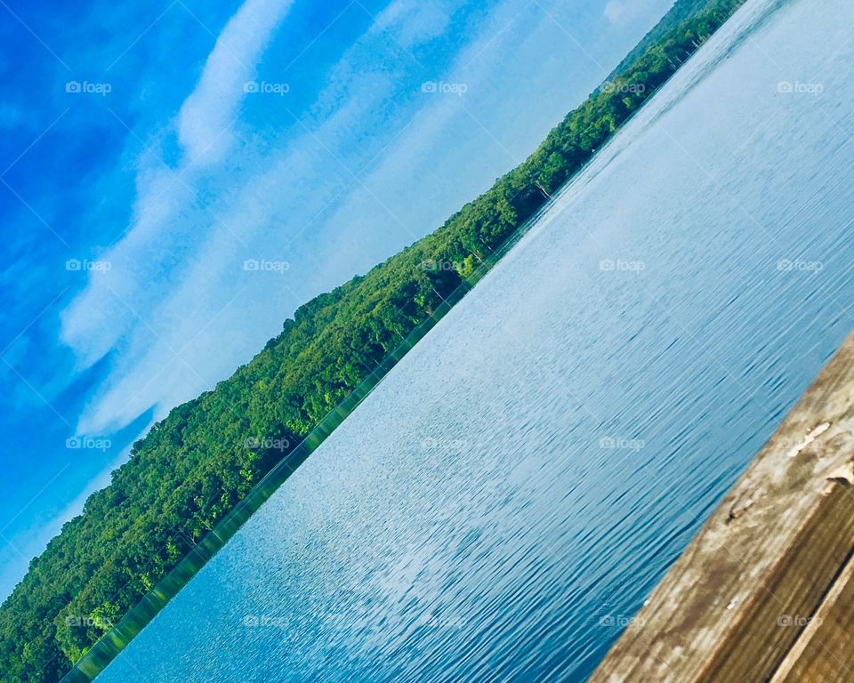 Good fishing lake on a beautiful sunny day. Water is reflecting the blue sky with puffs of clouds.