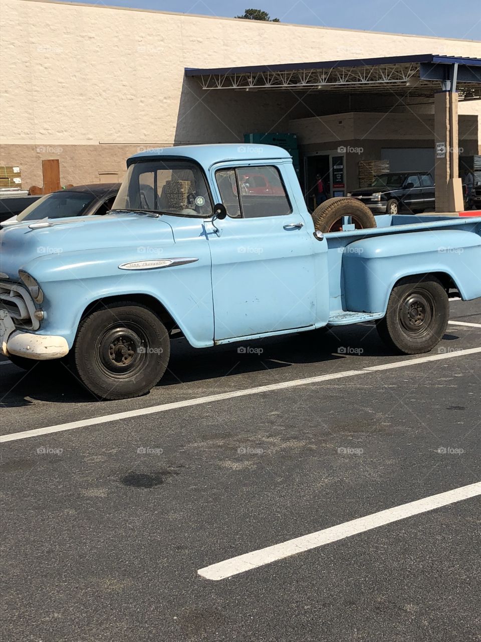 A baby blue old ford pick up truck in a parking lot. 