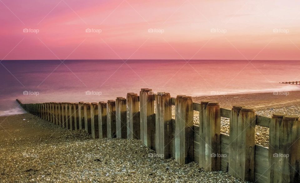Pinky purple sky just after sunset on pebbled beach with wooden breakers leading down to the calm sea 
