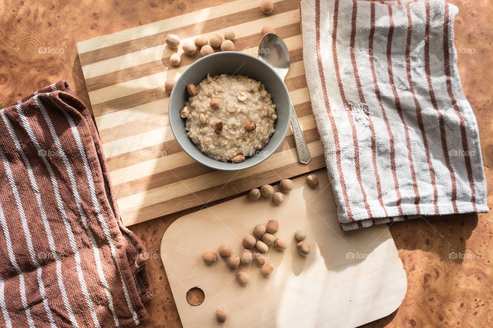 Cooked oatmeal in a deep gray plate with hazelnuts and honey.