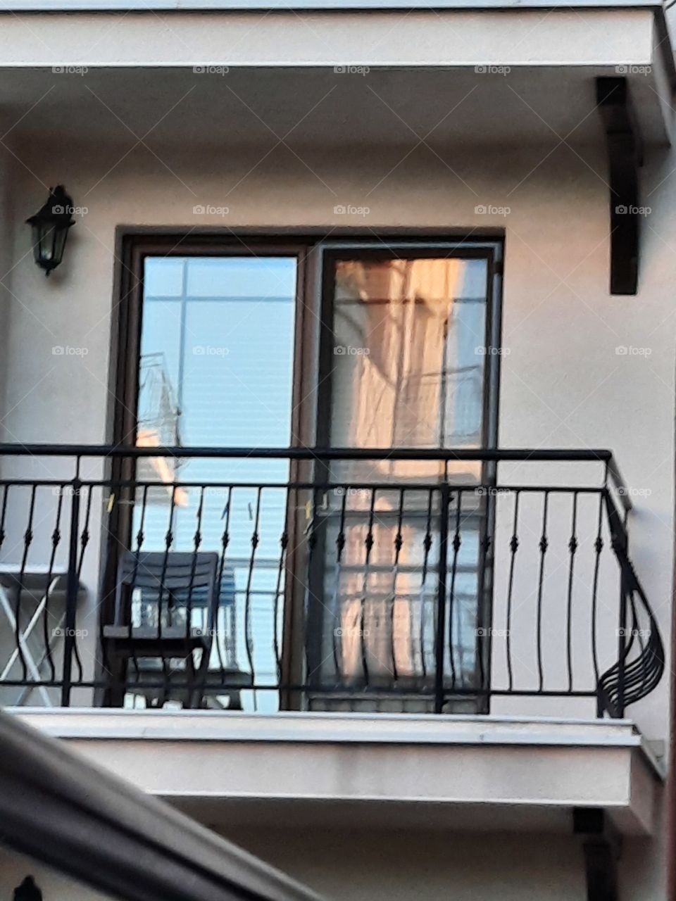 reflection of blue sky and sunlit buildingin the window of shady balcony