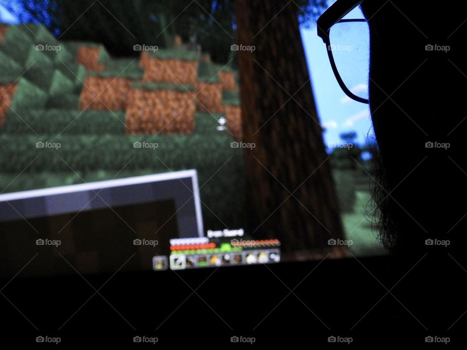 Teenager boy playing Minecraft on the gaming computer seen from his glasses close-up in a dark room.