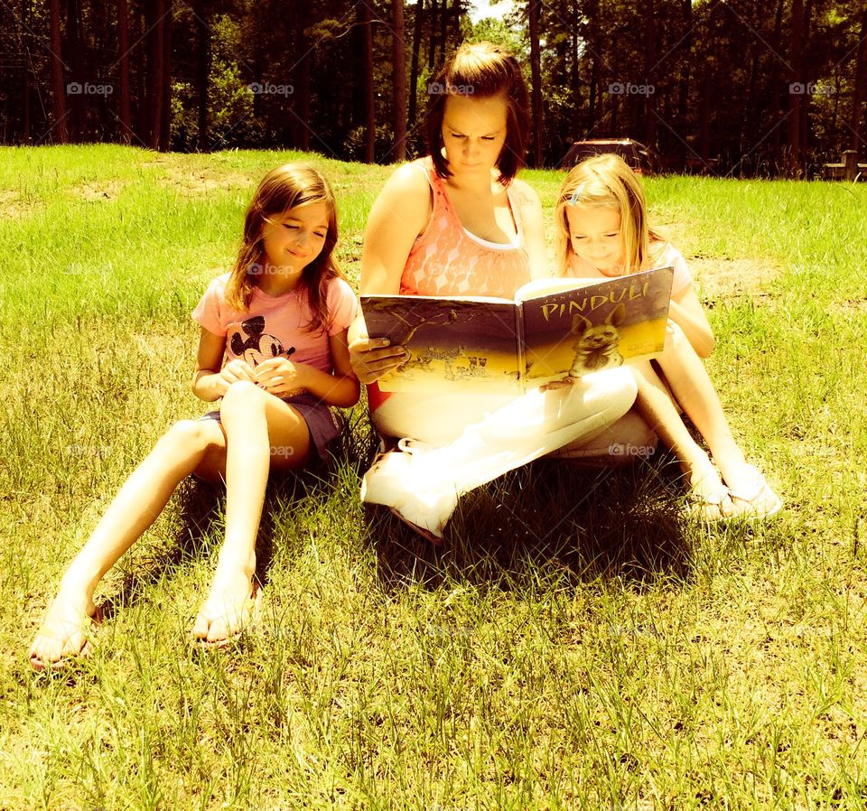 Mother and daughters in park reading story book