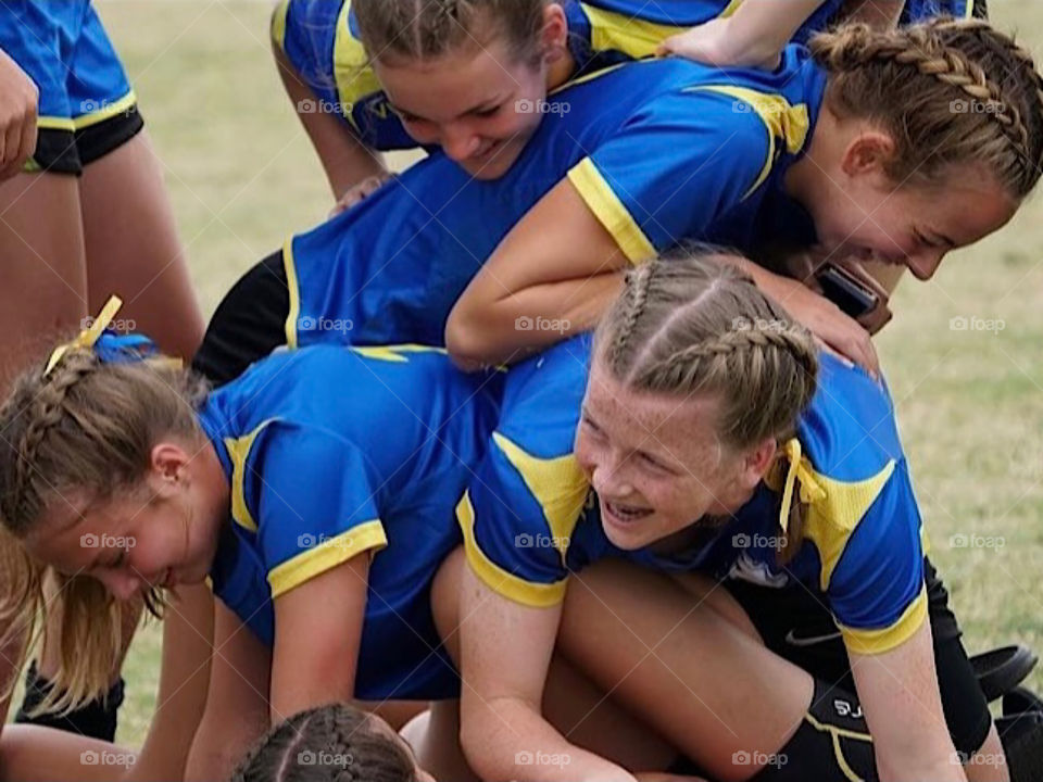 Excited girls stacking on top of each other after winning a football (soccer) game.