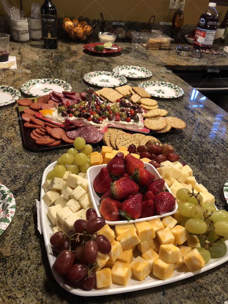 Holiday food spread of cheese and meats on a tray with crackers and strawberries and grapes. All flavors and fruits are so good. Christmas decor and plates for eating our snacks on. 