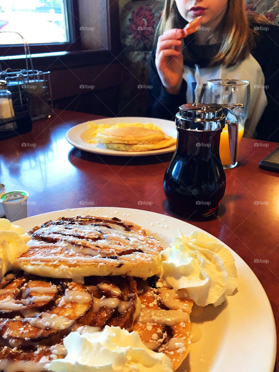 In the foreground; Cinnamon roll pancakes with sweet cream cheese sauce & whipped cream and across the table; pancakes, syrup and my daughter munching a piece of crispy bacon! We love brunch!!! 🥞