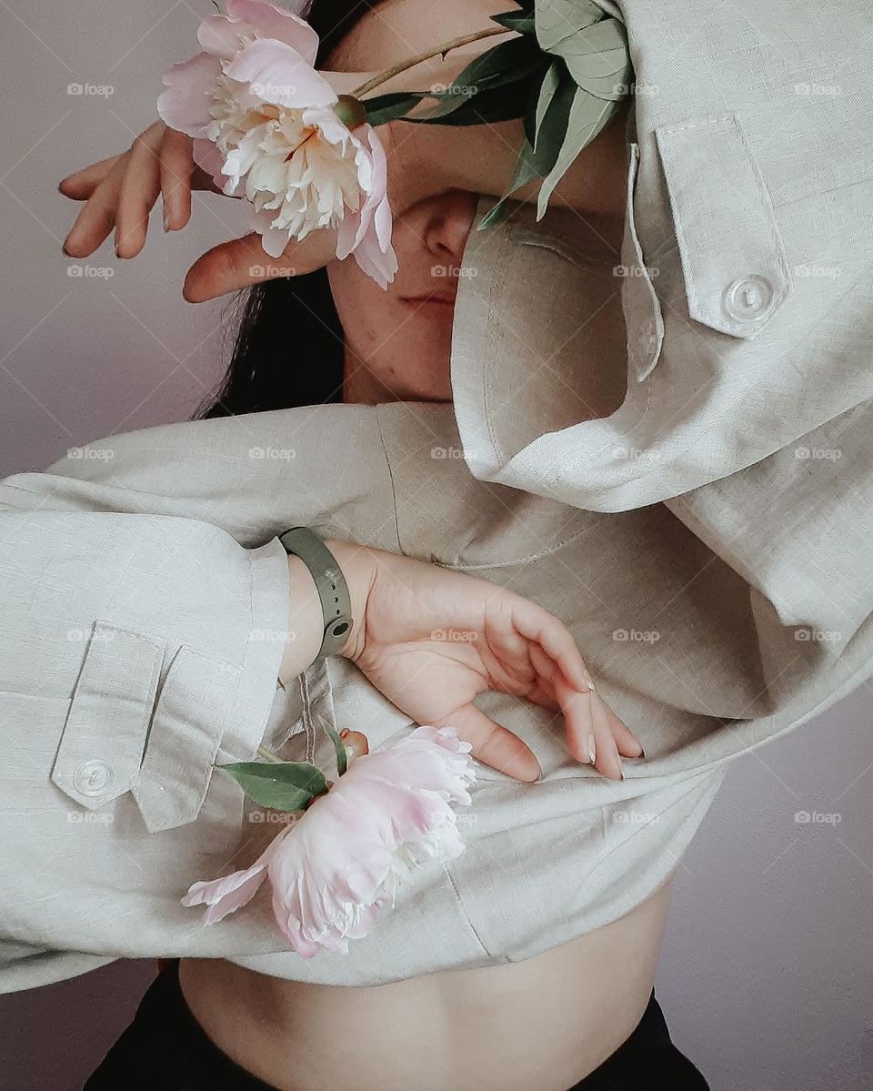 original portrait of a fair-skinned girl covering her face with a white blouse with pink peonies in her sleeves