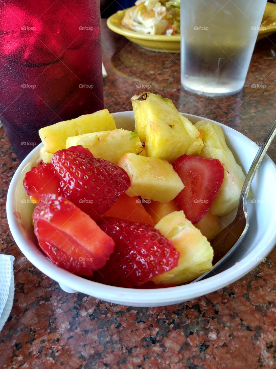 A nice cool fruit bowl with juicy red strawberries and tantalizing pineapple with a icy drink.