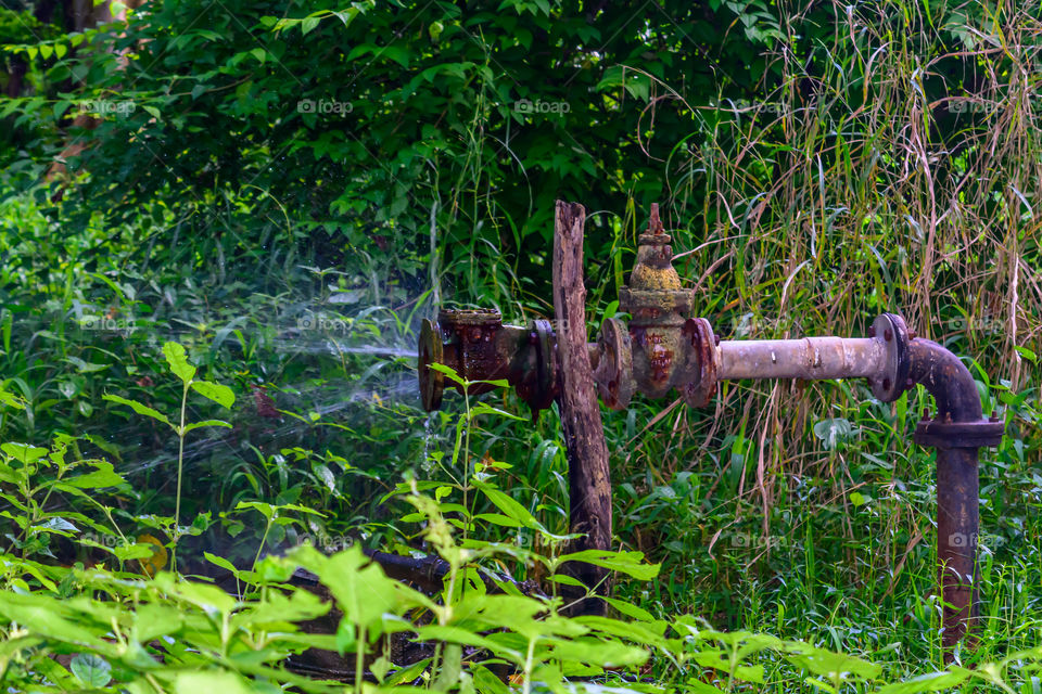 Old iron Metallic water pipe leaking. Rusty burst pipe spraying water.