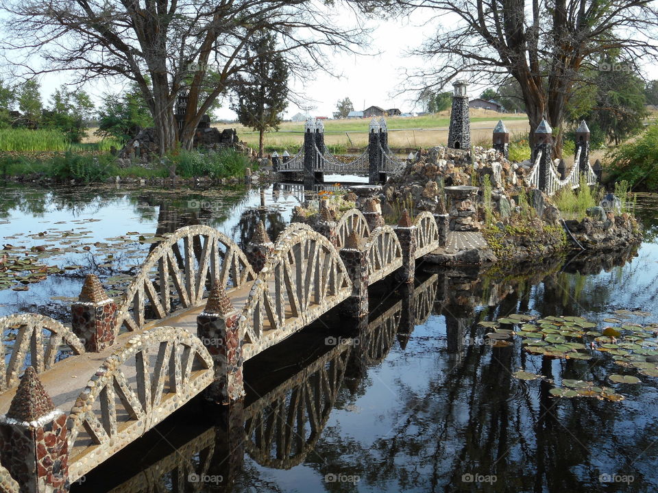 A beautiful and ornate rock bridge on a peaceful path crosses a fairytale style mote with lots of Lillie Pads at Peterson’s Rock Garden on a sunny summer day in Central Oregon. 