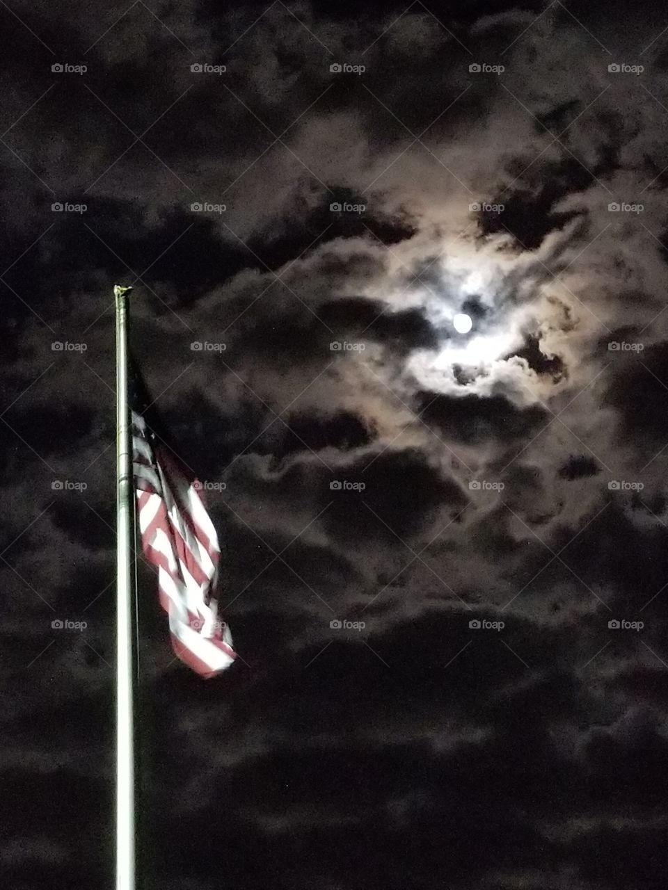 Old Glory in the light of the moon, American flag shines under a clouded sky