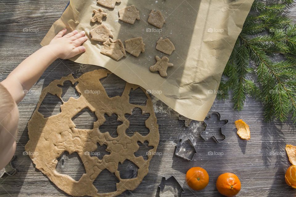 A small child helps to prepare festive, gingerbread cookies on a wooden table on Christmas Eve.