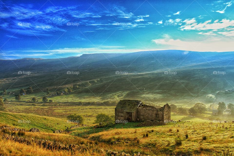 A deep valley cuts through green countryside with a deserted barn on its slopes.