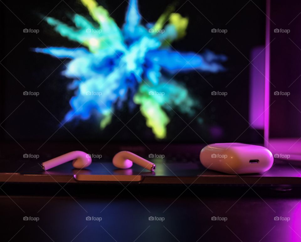 Air pods on a desk with pink lighting in the background 
