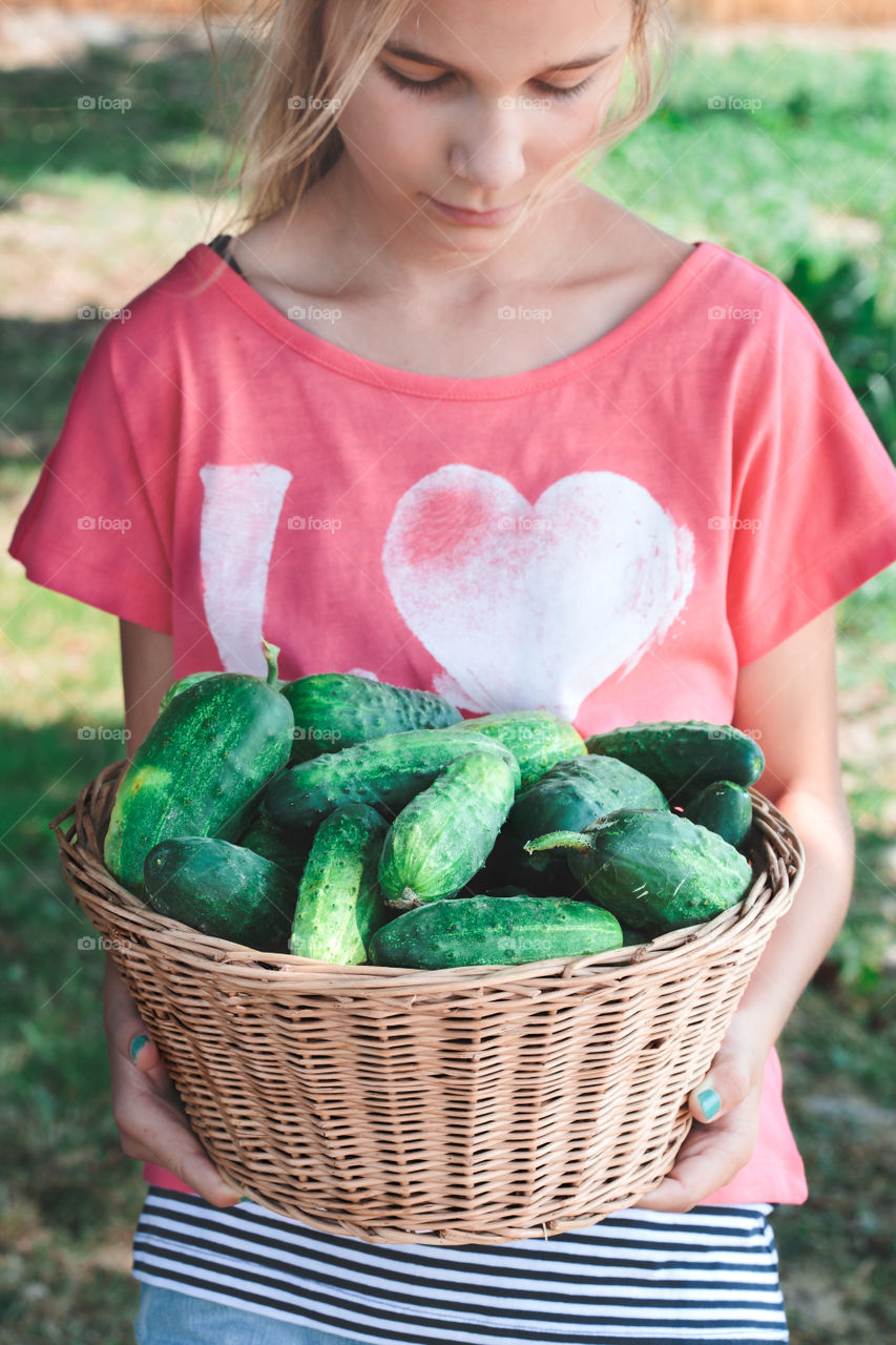 Girl carrying cucumbers. Girl carrying wicker basket with cucumbers