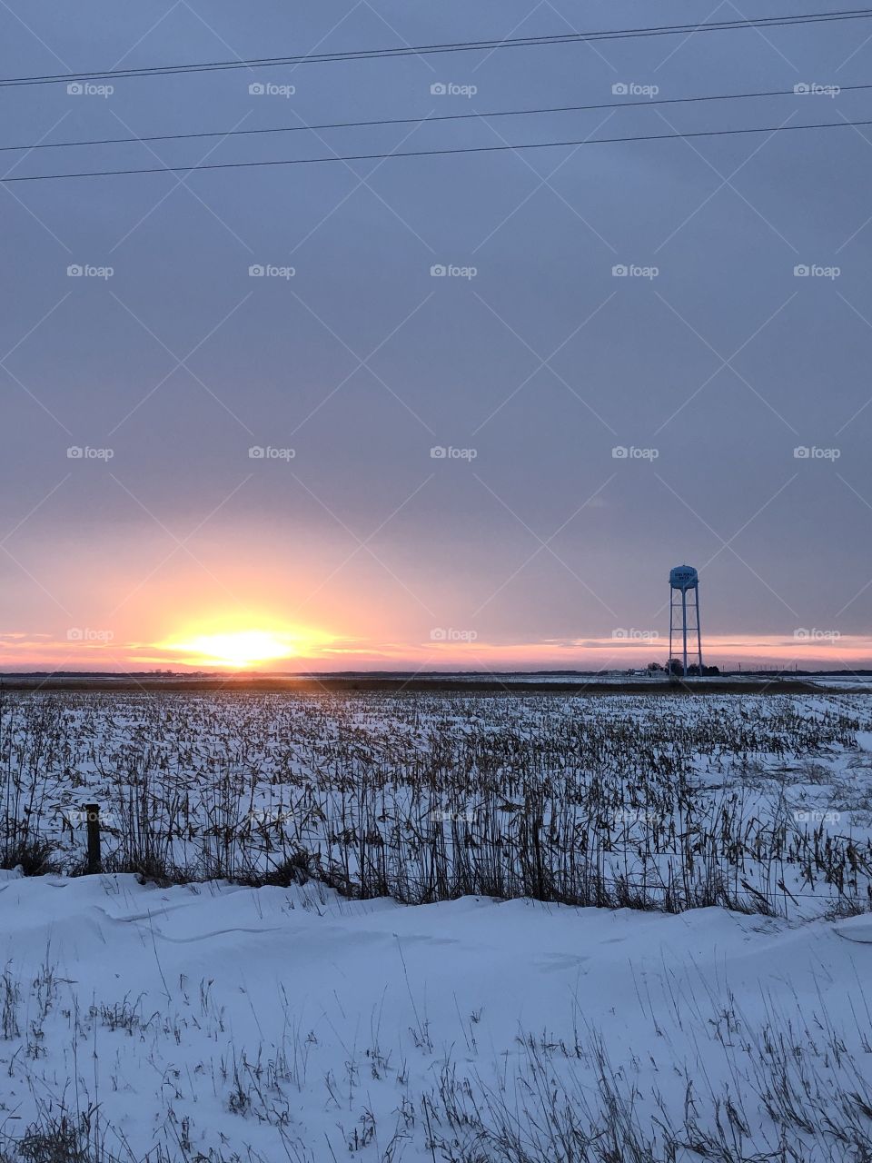 Sunset over the snow covered cornfield water tower standing in the background 