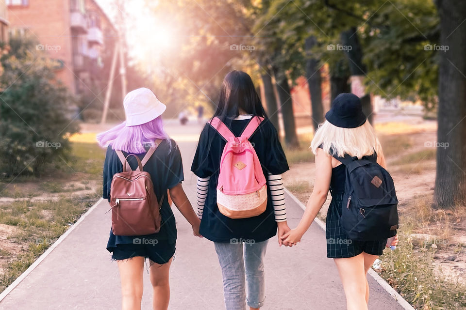 Three friends walking together with backpacks by the autumn city street 