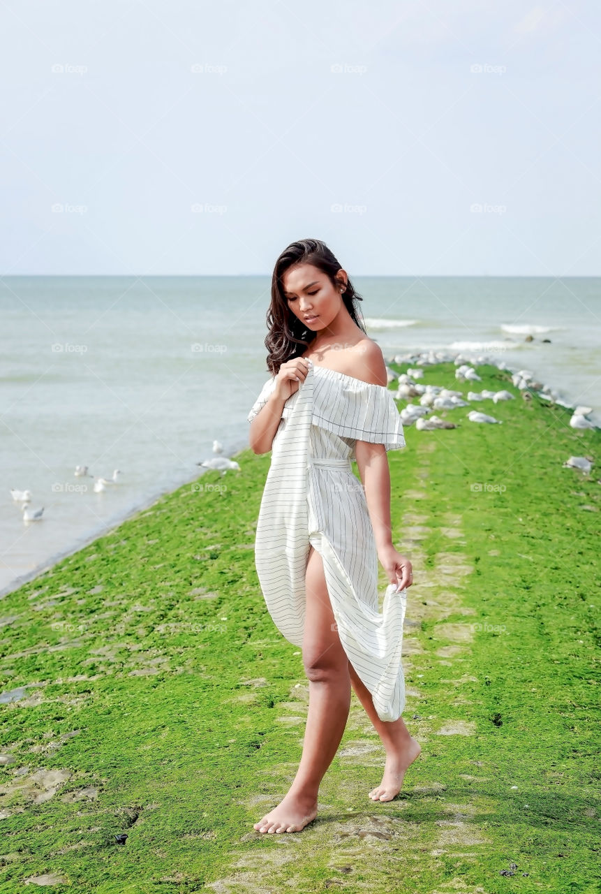 Asian woman walking on mossy pier near the sea