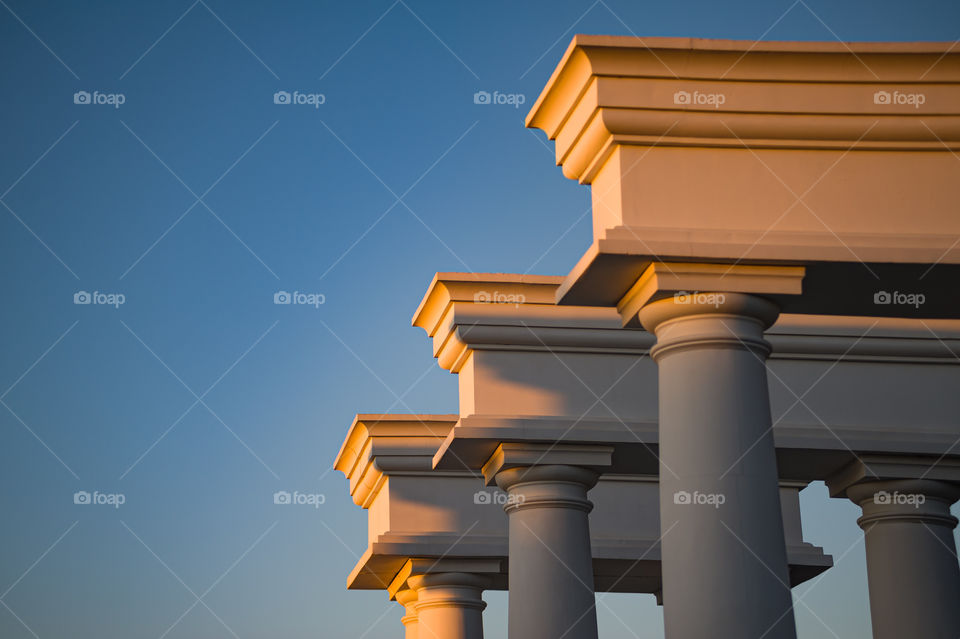 three white columns painted with golden paint of sunset against a blue sky