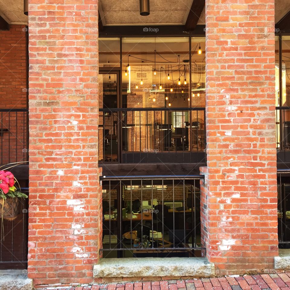 And interior workspace is visible through large picture glass windows from the outside. It is framed by two brick columns and an iron railing.