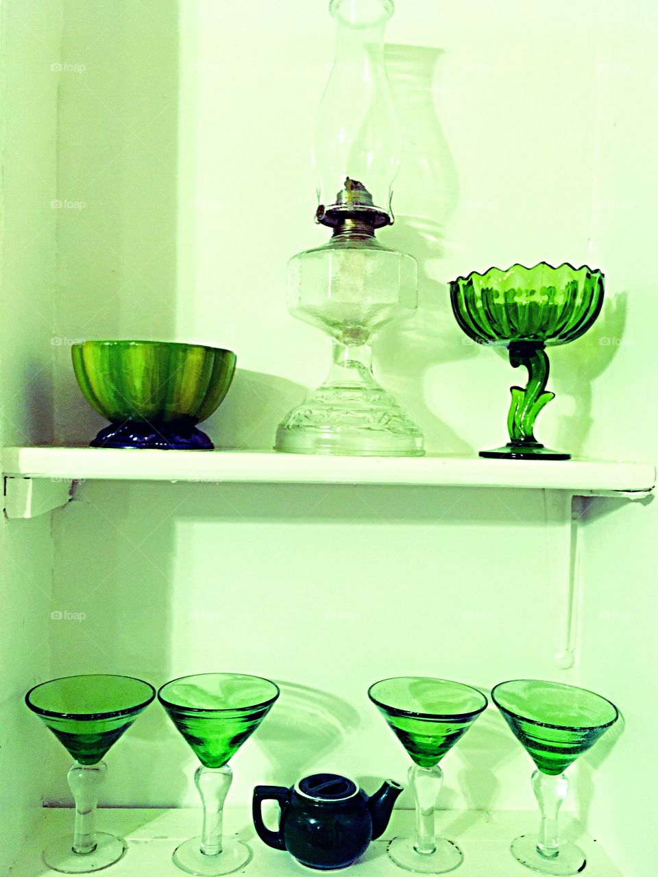 Antique green glassware. Oil lamp, martini glasses, dishes on white shelves. 