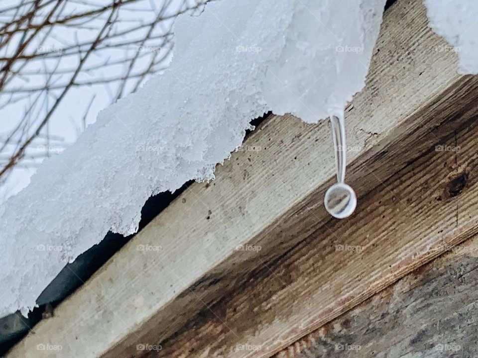 A drop of water falling from melting snow and ice on the roof overhang of a wooden structure 