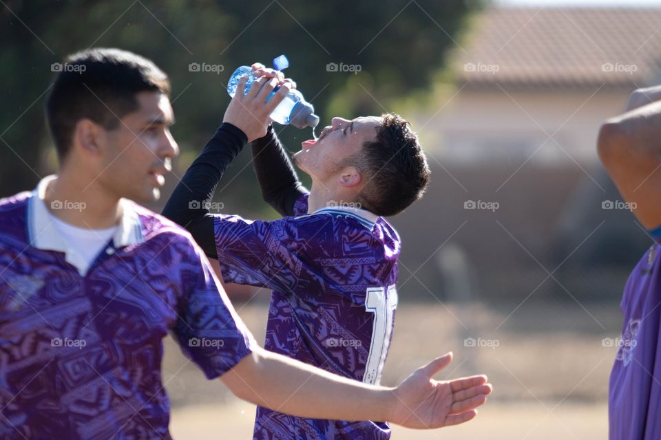 Jogador de futebol tomando água em dia ensolarado.