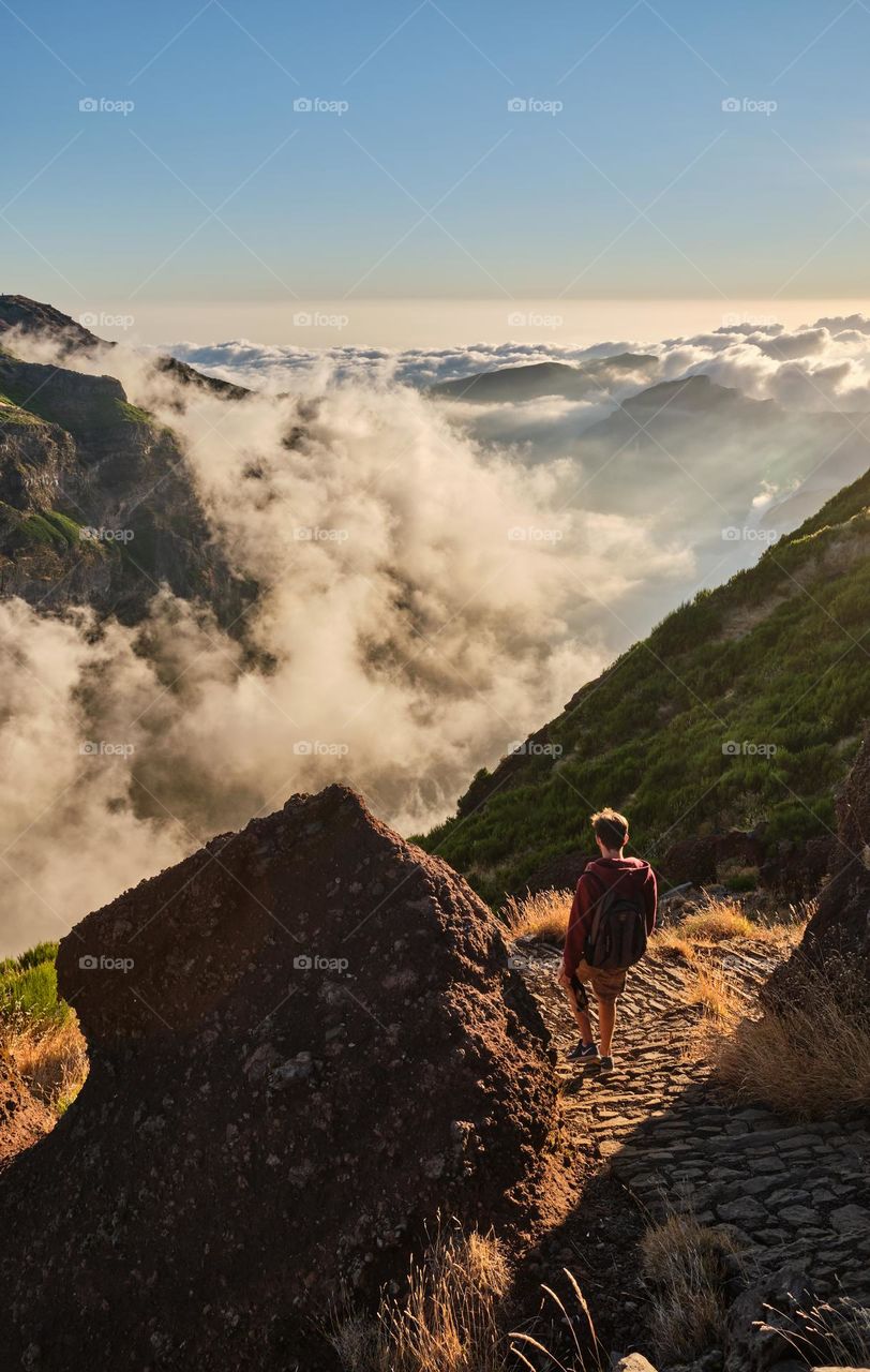 A boy is watching the Sunset over the clouds at highest maintains of Madeira island 