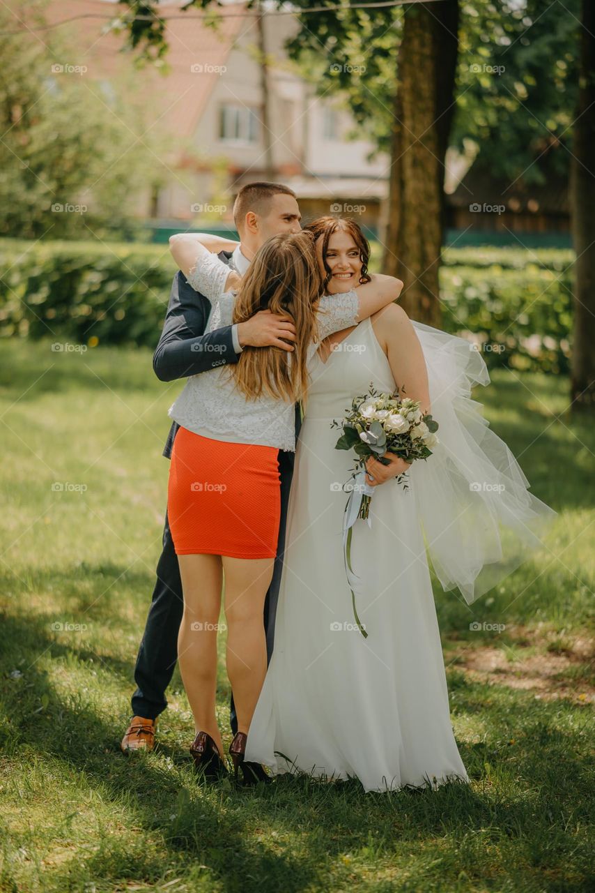 The moment of happy hugs of a friend with the bride and groom