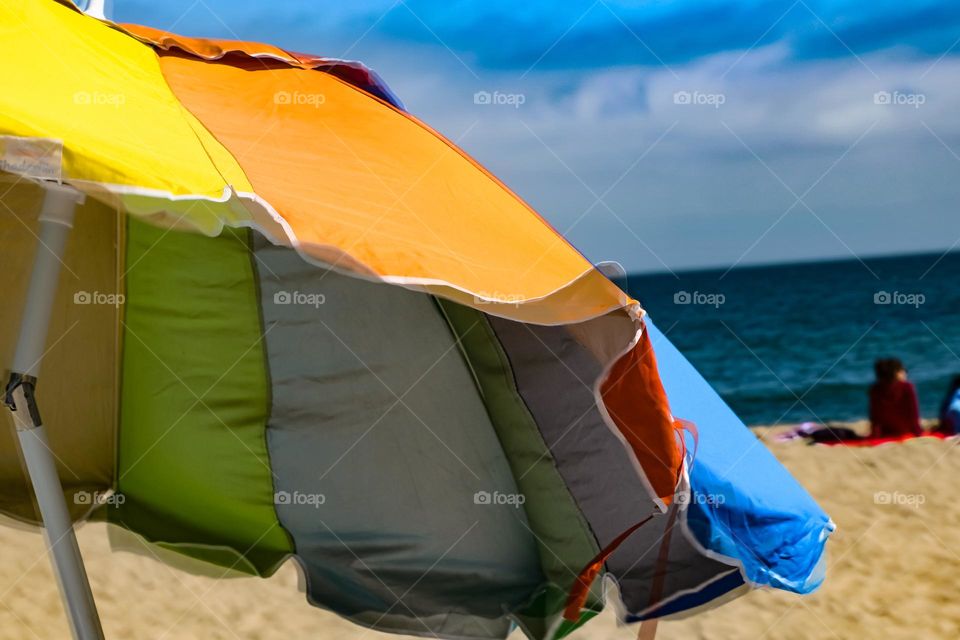 Colorful beach umbrella flapping in the wind on a beautiful day at the beach, with clear skies and calm waters 