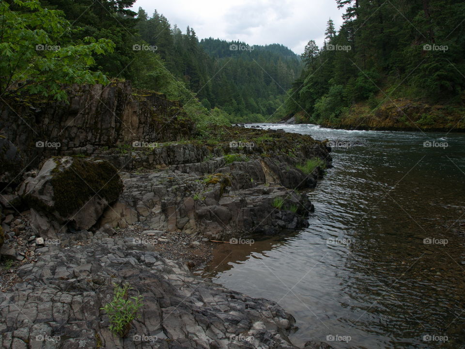 Boulders and rocks line the river banks of the magnificent waters of the Umpqua River in Southwestern Oregon on a summer morning. 