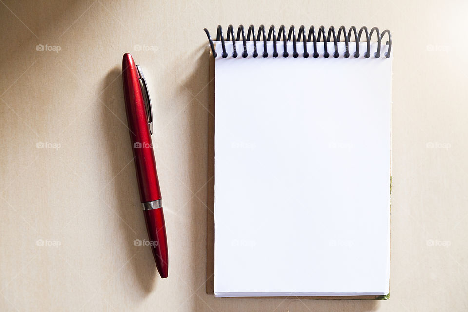 Blank notepad on the wooden table, with a red pen at the side, with sunlight hitting the side. Notepad for noting reminders. Annotation concept. Object concept. Copy space