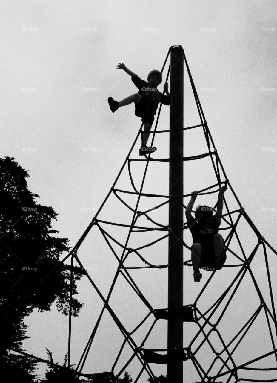 Children Climbing Ropes. Silhouette Of Children Climbing Tall Vertical Rope Structure At A Playground
