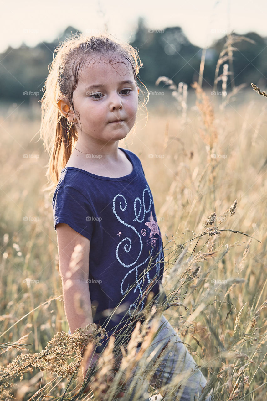 Little happy smiling girl playing in a tall grass in the countryside. Candid people, real moments, authentic situations