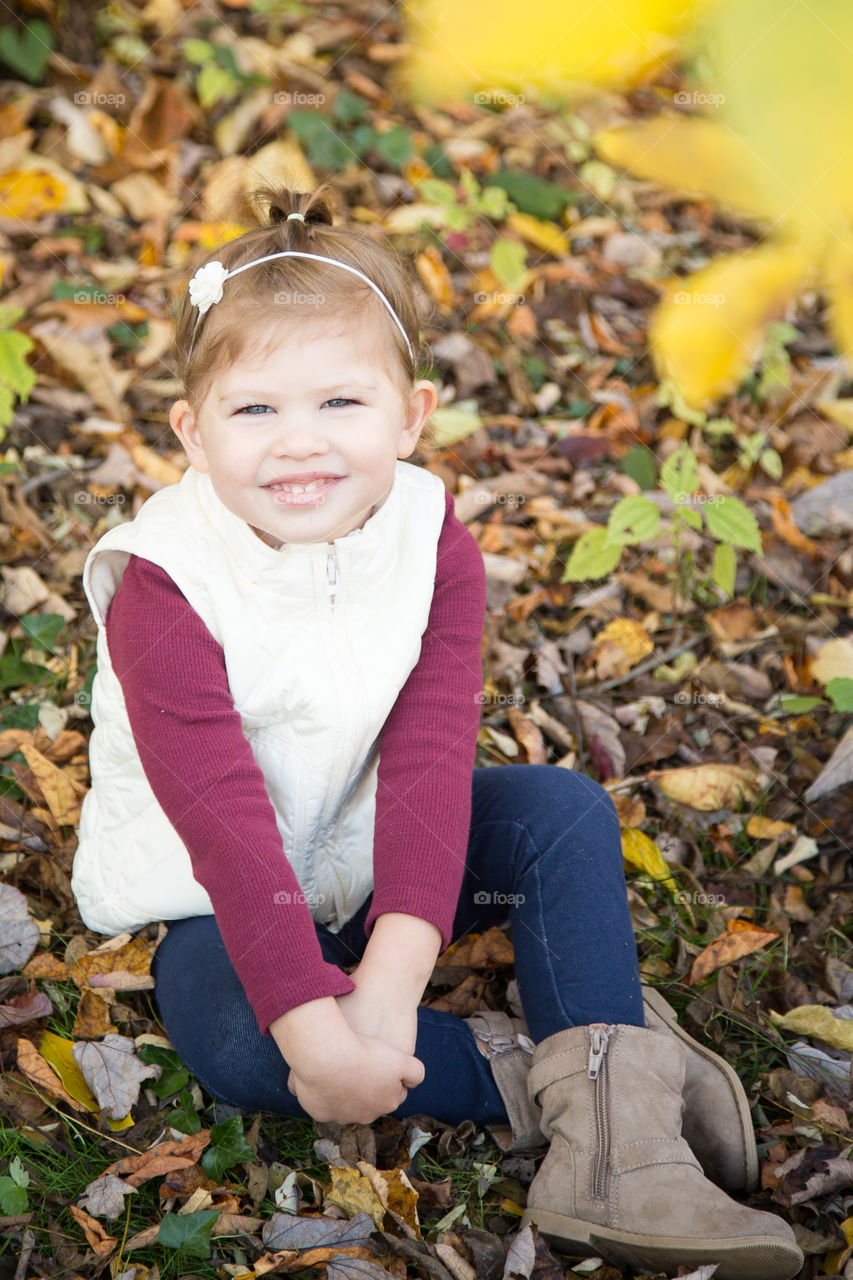 Smiling girl sitting on autumn dry leaves