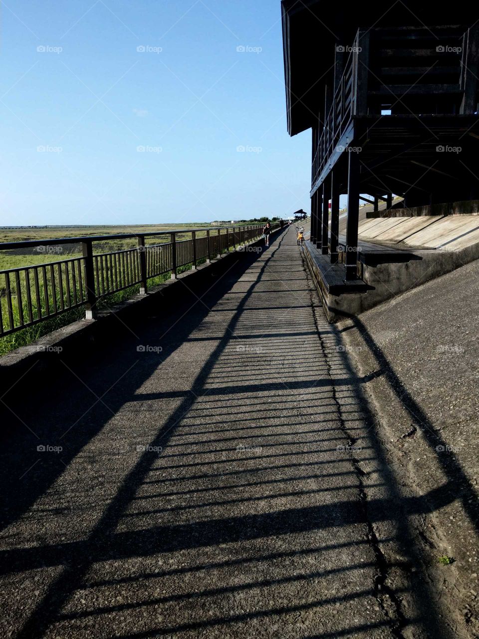 Silhouettes and shadows: long long road at seaside, long long embankment railing's shadow and an observatory at dusk.