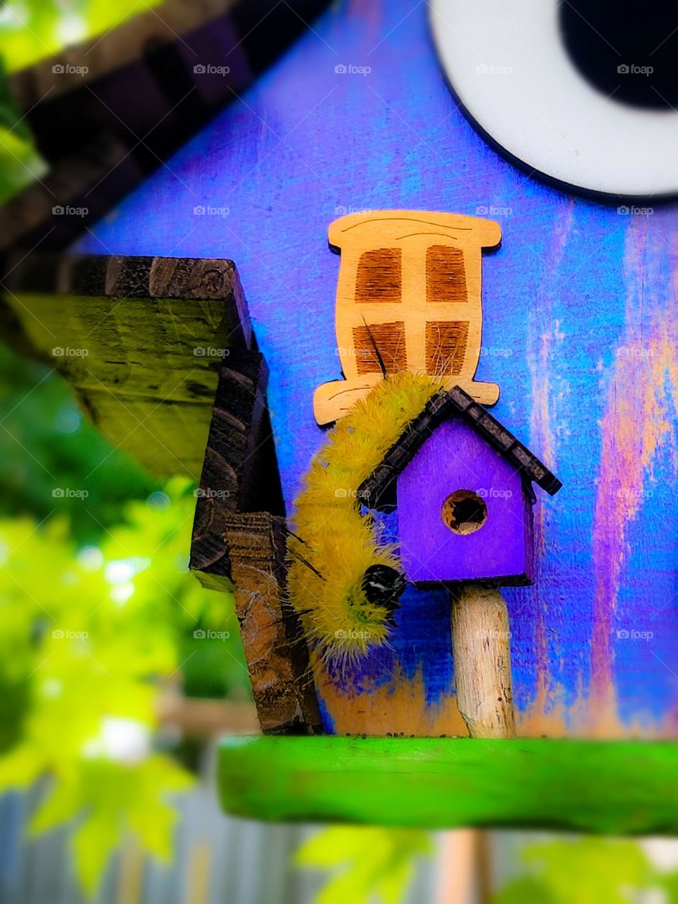 Fuzzy yellow caterpillar finding a home in a bright purple bird house.