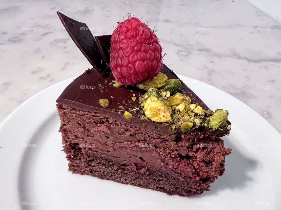 Side view of the tasty sweet chocolate cake triangle shaped slice with pistachios and raspberry 